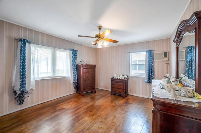 bedroom with a ceiling fan, a wall unit AC, hardwood / wood-style flooring, and baseboards
