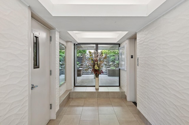 hallway with a raised ceiling, light tile patterned floors, and a wealth of natural light