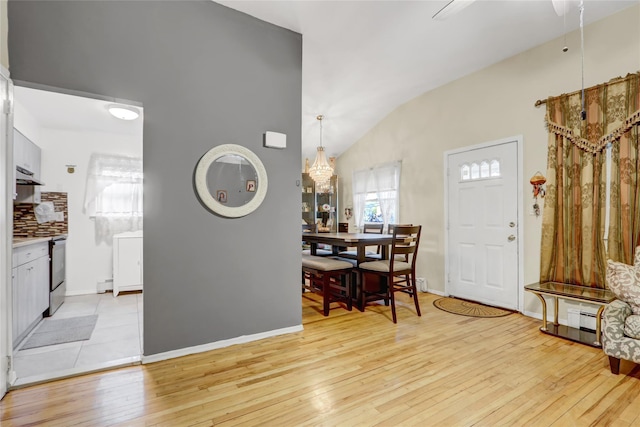 entryway featuring a baseboard heating unit, baseboards, vaulted ceiling, and light wood-type flooring