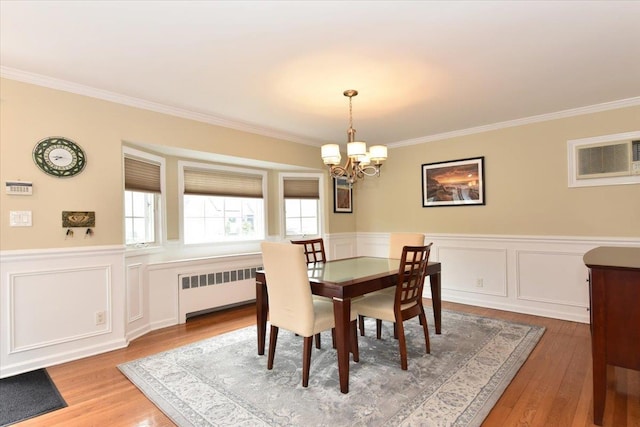 dining space with wood finished floors, wainscoting, radiator heating unit, ornamental molding, and a notable chandelier