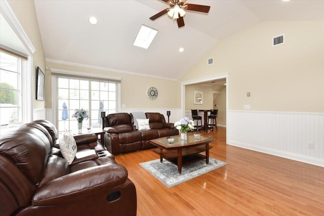 living room with a ceiling fan, visible vents, wainscoting, and light wood-style flooring
