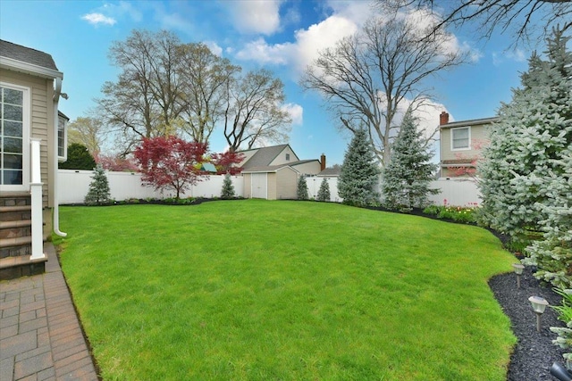 view of yard featuring entry steps, a fenced backyard, an outbuilding, and a storage shed
