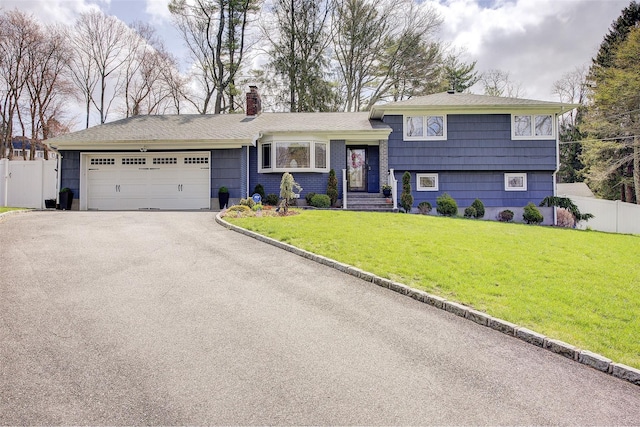 tri-level home featuring fence, an attached garage, a front lawn, a chimney, and driveway