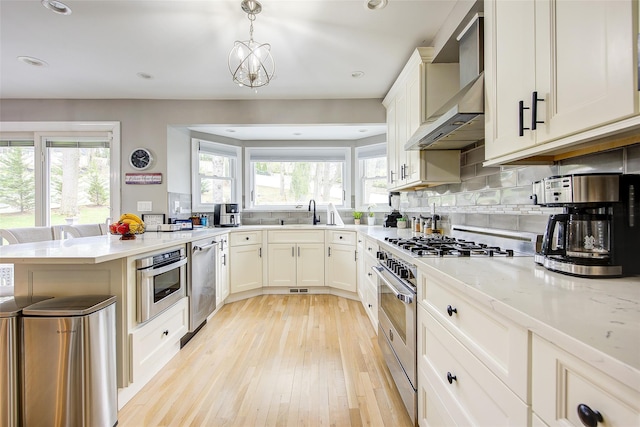 kitchen with wall chimney range hood, appliances with stainless steel finishes, a peninsula, recessed lighting, and light wood-style flooring