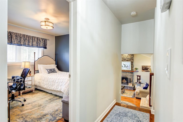 bedroom with baseboards, a stone fireplace, and wood finished floors
