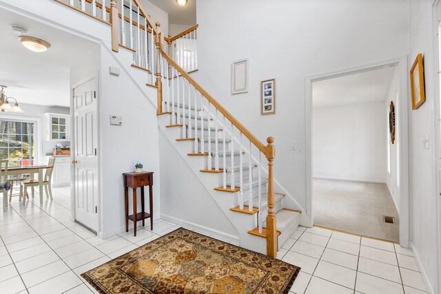 stairs with tile patterned flooring, baseboards, an inviting chandelier, a high ceiling, and carpet flooring