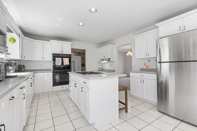 kitchen with dobule oven black, a center island, light tile patterned floors, white cabinets, and freestanding refrigerator
