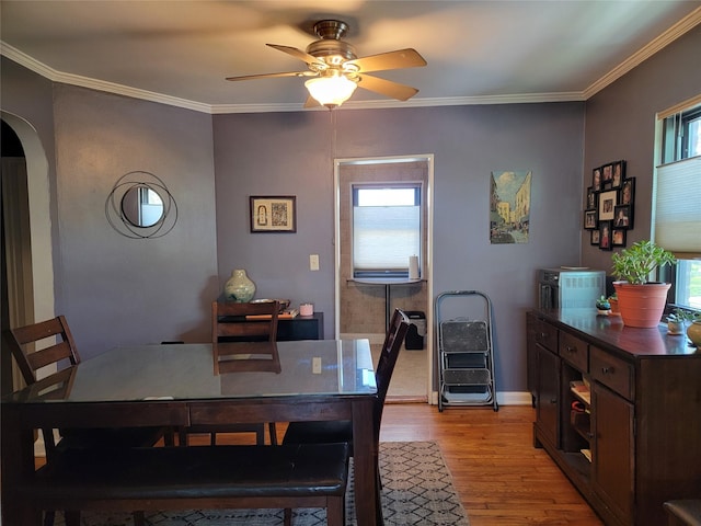 dining space featuring ceiling fan, light wood-style floors, arched walkways, baseboards, and ornamental molding