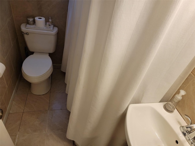 bathroom with toilet, tile patterned floors, tile walls, and a sink