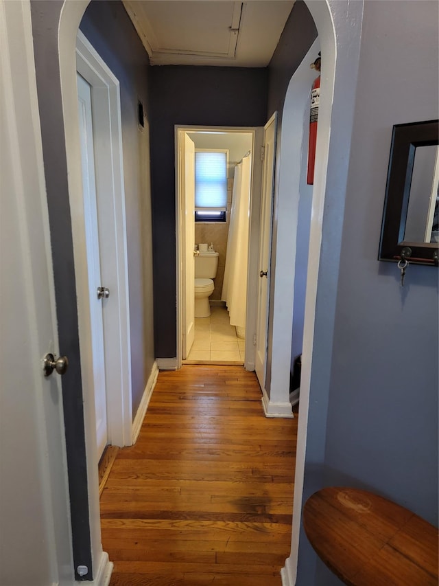 hallway featuring baseboards, arched walkways, and light wood finished floors