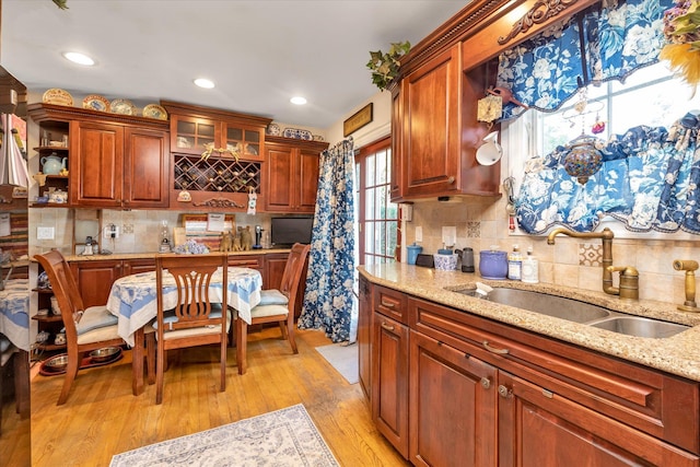 kitchen featuring a sink, tasteful backsplash, light wood-style flooring, light stone countertops, and glass insert cabinets