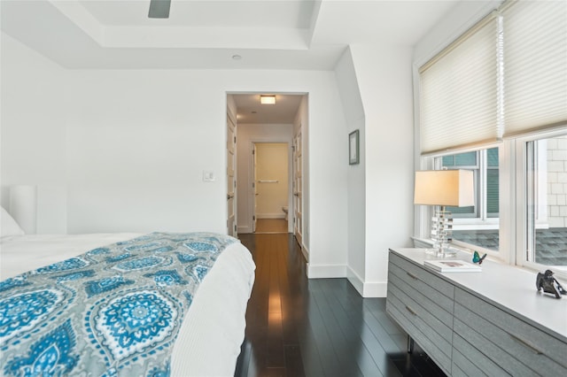 bedroom with baseboards, a raised ceiling, and dark wood-type flooring