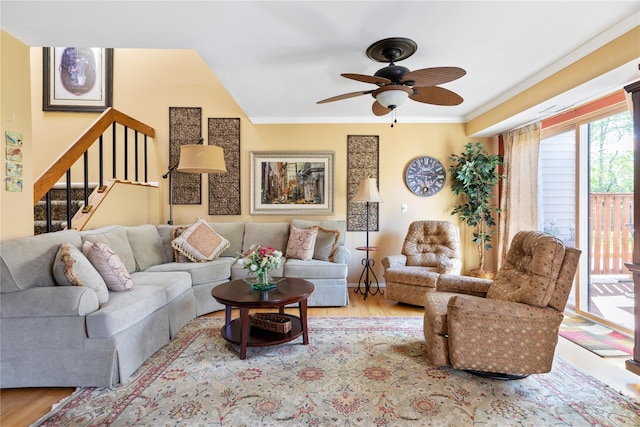 living area with crown molding, ceiling fan, wood finished floors, and stairway