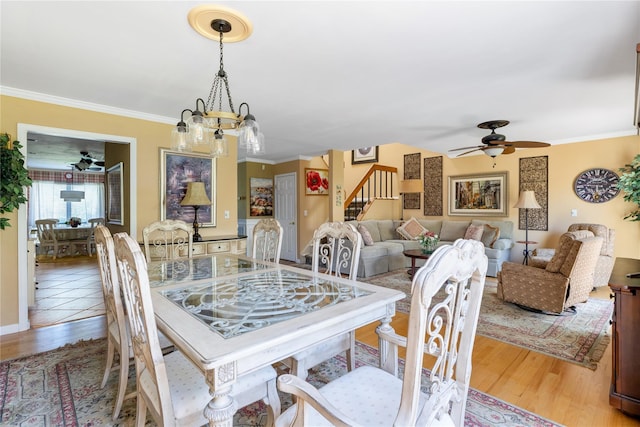 dining space featuring stairway, ornamental molding, ceiling fan with notable chandelier, and wood finished floors