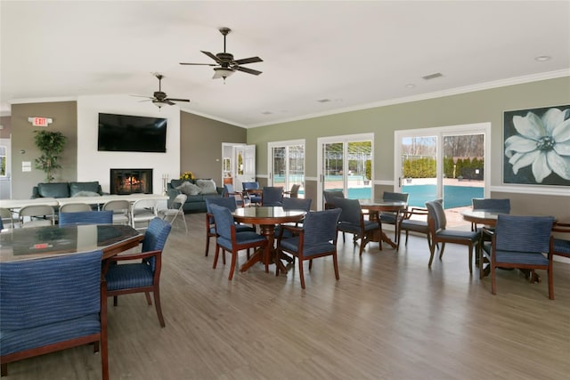 dining area featuring ceiling fan, visible vents, crown molding, a fireplace, and light wood-style floors
