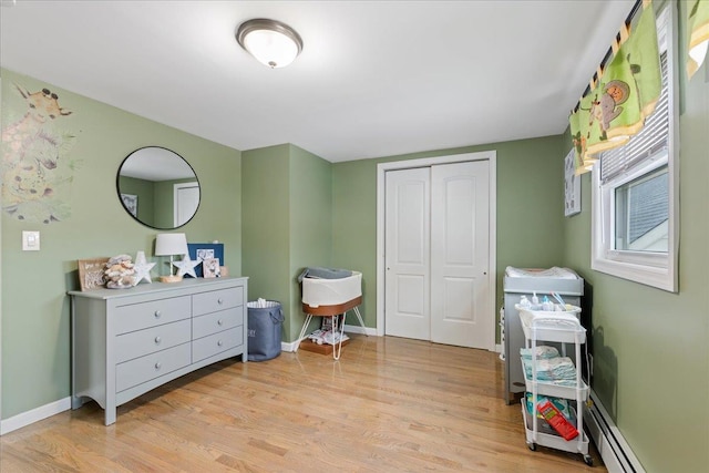 bedroom with baseboards, a closet, baseboard heating, and light wood-style floors