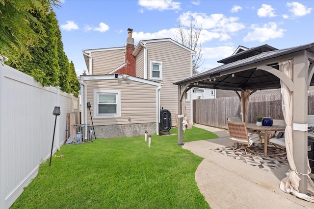 rear view of house featuring a patio, a yard, a fenced backyard, a chimney, and a gazebo