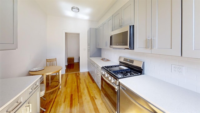 kitchen featuring light wood-style floors, light countertops, stainless steel appliances, backsplash, and gray cabinetry