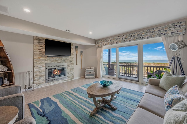 living room featuring a stone fireplace, wood finished floors, and visible vents