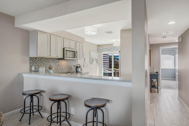kitchen featuring stainless steel microwave, visible vents, baseboards, and light wood-type flooring