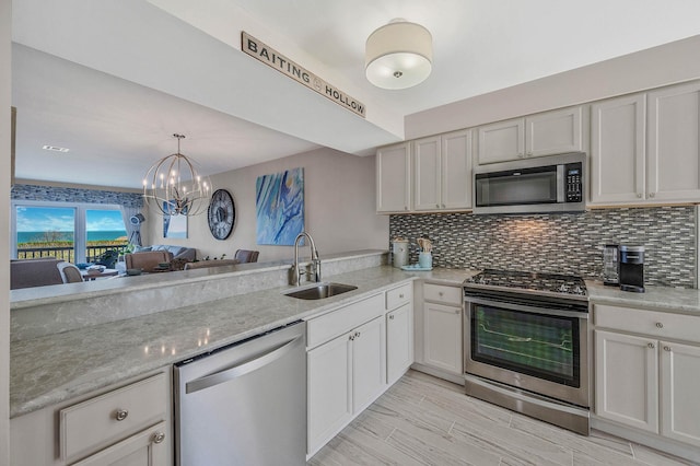 kitchen with light stone counters, appliances with stainless steel finishes, a sink, tasteful backsplash, and pendant lighting
