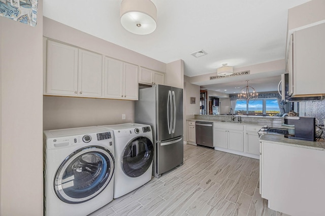 laundry area with laundry area, visible vents, a sink, light wood-style floors, and separate washer and dryer