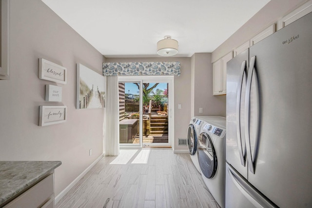clothes washing area featuring visible vents, washing machine and dryer, baseboards, light wood-type flooring, and cabinet space
