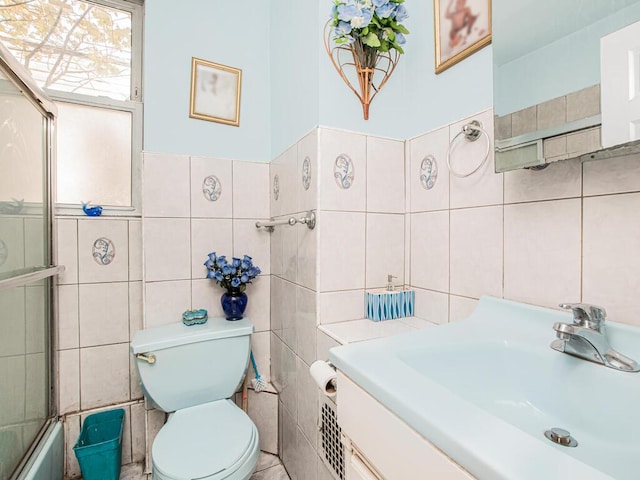 bathroom with a sink, toilet, shower / bath combination with glass door, and tile walls