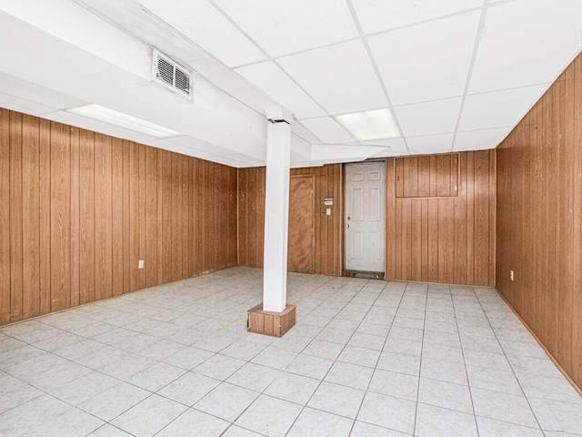 finished basement with wooden walls, light tile patterned floors, visible vents, and a drop ceiling