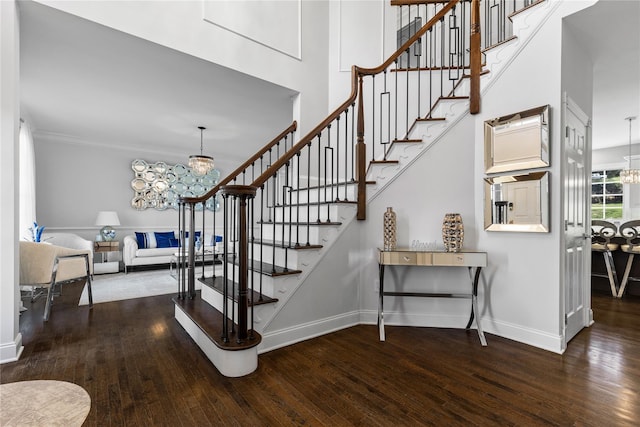 stairway with an inviting chandelier, wood finished floors, ornamental molding, and baseboards