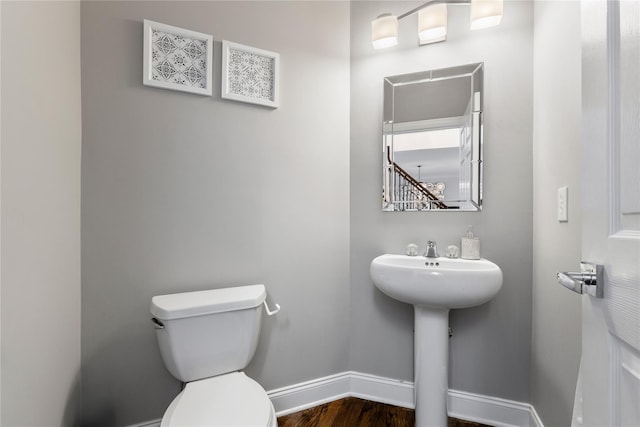 half bathroom featuring a sink, wood finished floors, toilet, and baseboards
