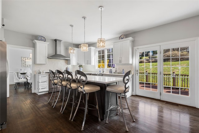 kitchen featuring a breakfast bar area, light countertops, white cabinetry, and wall chimney exhaust hood