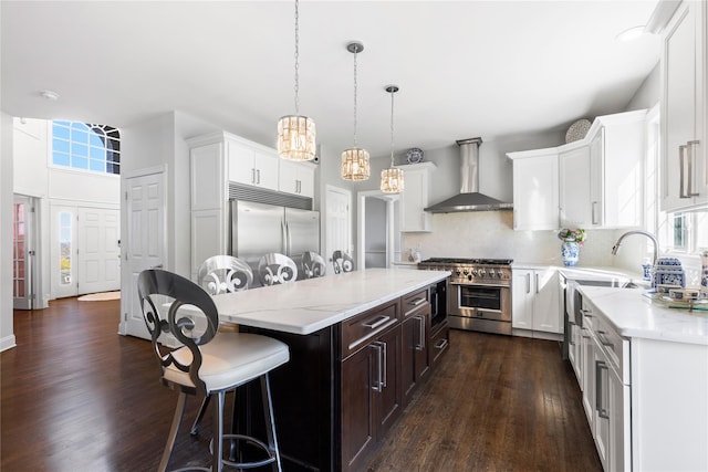 kitchen featuring wall chimney range hood, premium appliances, a healthy amount of sunlight, a kitchen island, and dark wood-style flooring