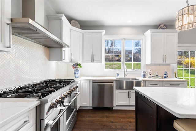 kitchen featuring tasteful backsplash, appliances with stainless steel finishes, wall chimney range hood, a sink, and white cabinetry