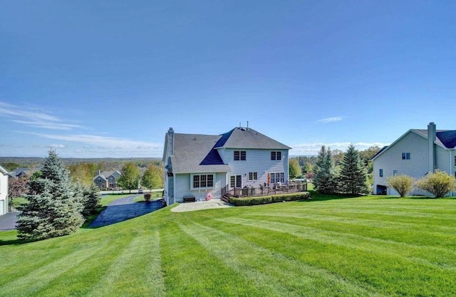 back of house with a chimney, a wooden deck, and a lawn