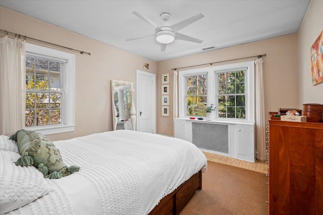 bedroom featuring a ceiling fan, radiator heating unit, visible vents, and wood finished floors