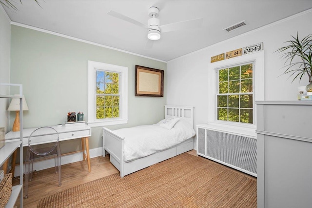 bedroom with wood finished floors, a ceiling fan, visible vents, ornamental molding, and radiator heating unit