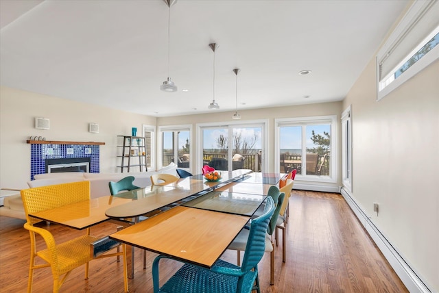 dining space featuring a wealth of natural light, baseboard heating, a tiled fireplace, and wood finished floors