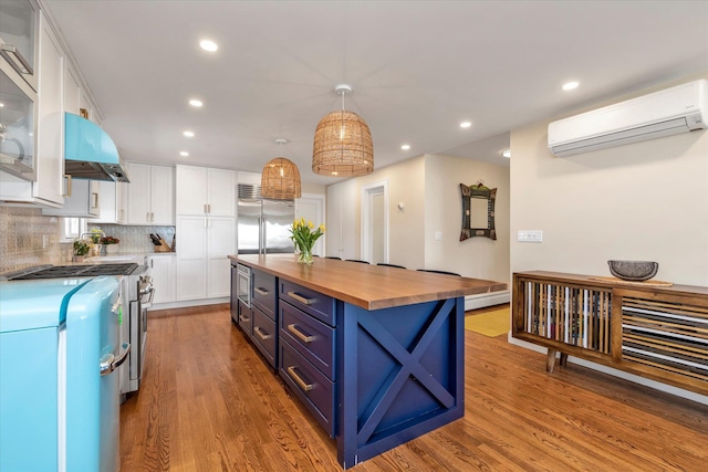 kitchen featuring butcher block counters, high end appliances, a wall mounted air conditioner, white cabinetry, and blue cabinetry