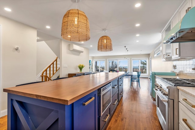 kitchen featuring wooden counters, blue cabinets, wood finished floors, high end stainless steel range, and under cabinet range hood