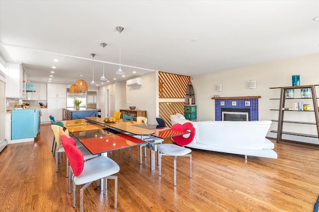 dining space with recessed lighting, light wood-type flooring, a wall mounted air conditioner, and a tile fireplace