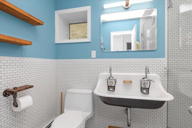 bathroom with a sink, tile walls, wainscoting, and toilet