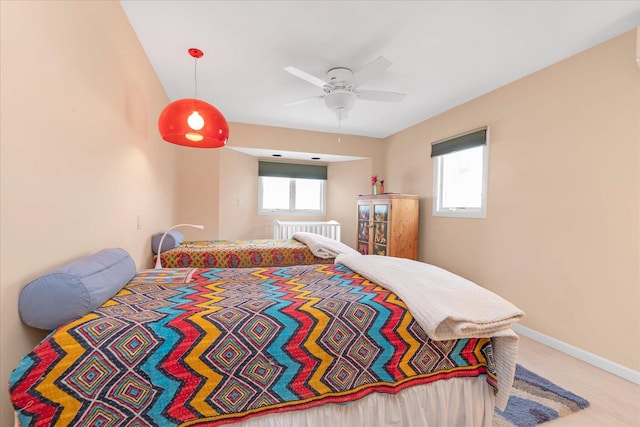 bedroom with radiator heating unit, baseboards, multiple windows, and a ceiling fan