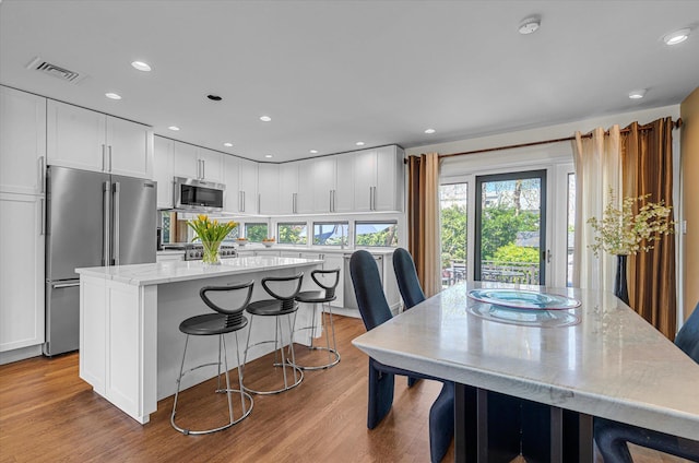 kitchen with appliances with stainless steel finishes, a kitchen island, wood finished floors, and white cabinetry