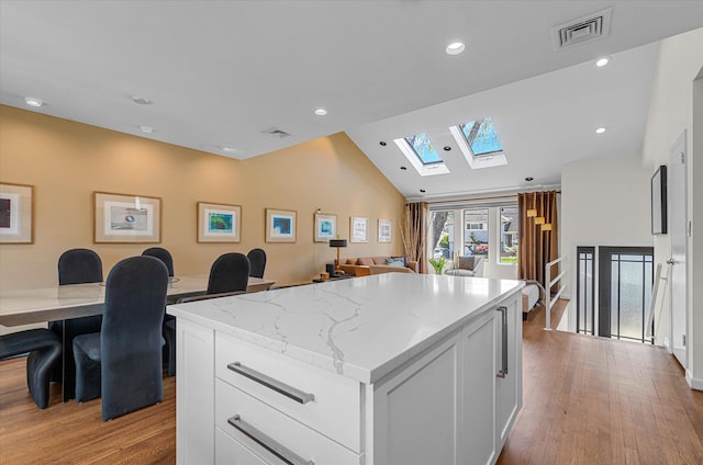 kitchen with a kitchen island, visible vents, lofted ceiling with skylight, light wood-style floors, and white cabinetry
