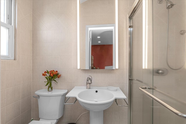 bathroom featuring toilet, tile walls, a sink, and a stall shower