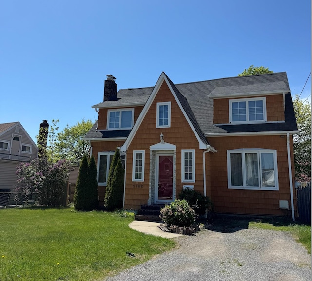 tudor-style house with roof with shingles, fence, a front yard, and a chimney