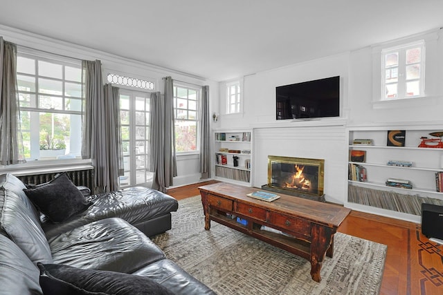 living area featuring plenty of natural light, a glass covered fireplace, built in features, and wood finished floors