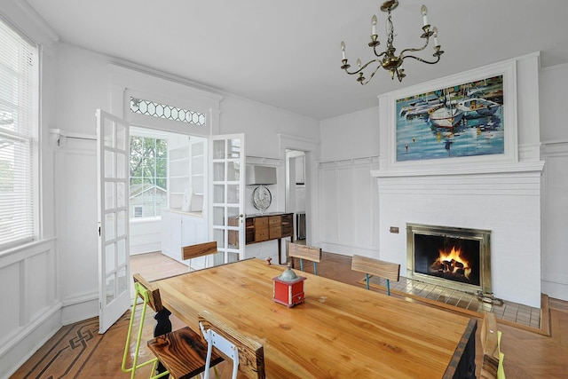 dining area with a decorative wall, a fireplace with flush hearth, a chandelier, wainscoting, and french doors