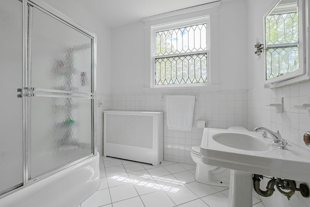 bathroom featuring radiator, tile walls, healthy amount of natural light, tile patterned flooring, and combined bath / shower with glass door
